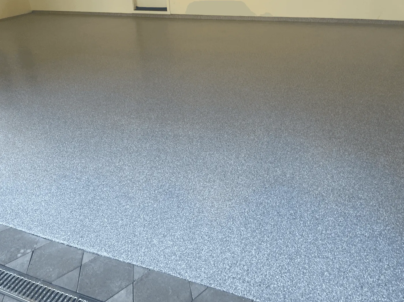 Pearl flake floor meeting hexagon pavers and a trench drain at a Seattle-area garage bay