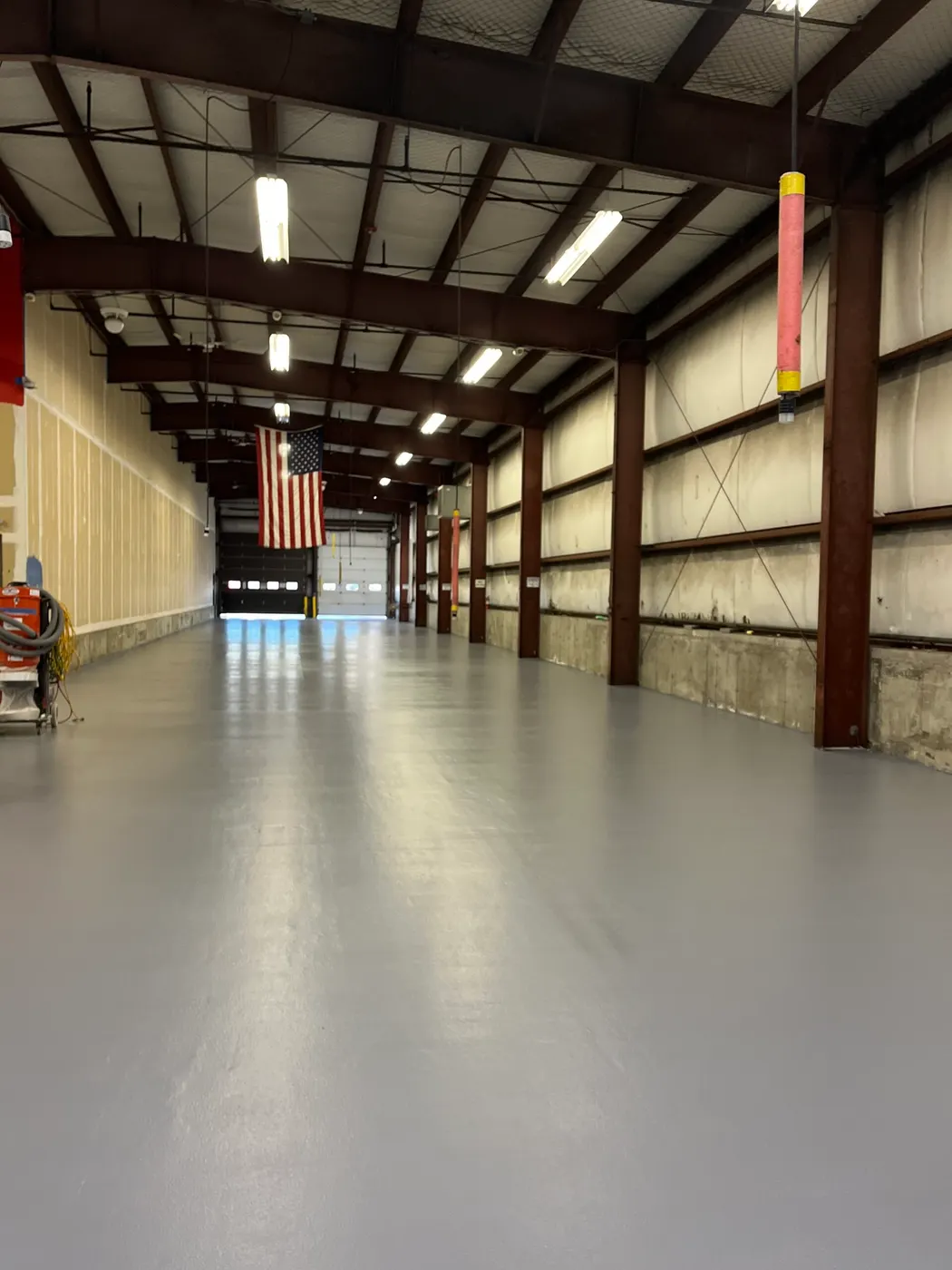 Long steel-framed commercial building with a gray floor coating and a hanging American flag