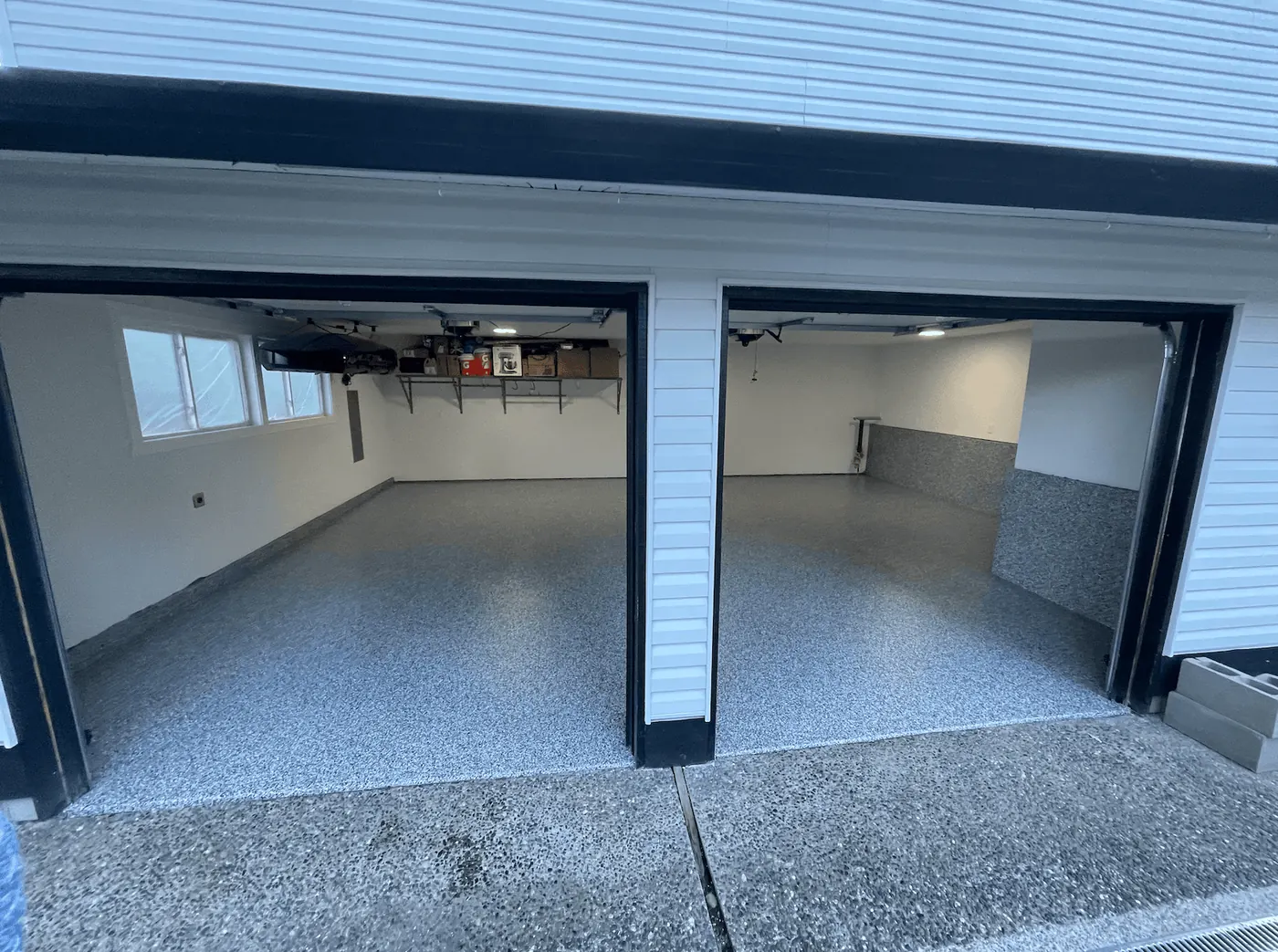 Two open garage bays in a white-sided Seattle-area home with a blue granite flake floor