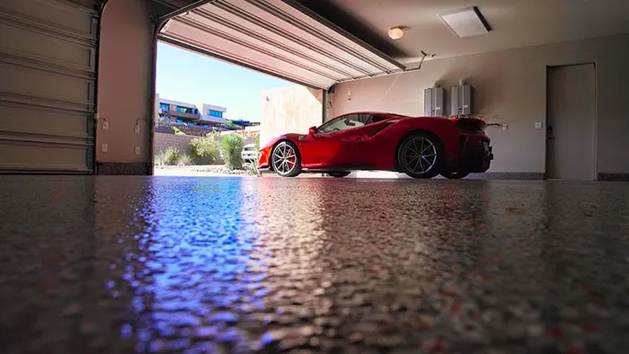 Low-angle view across a dark flake garage floor to a red Ferrari outside the open door