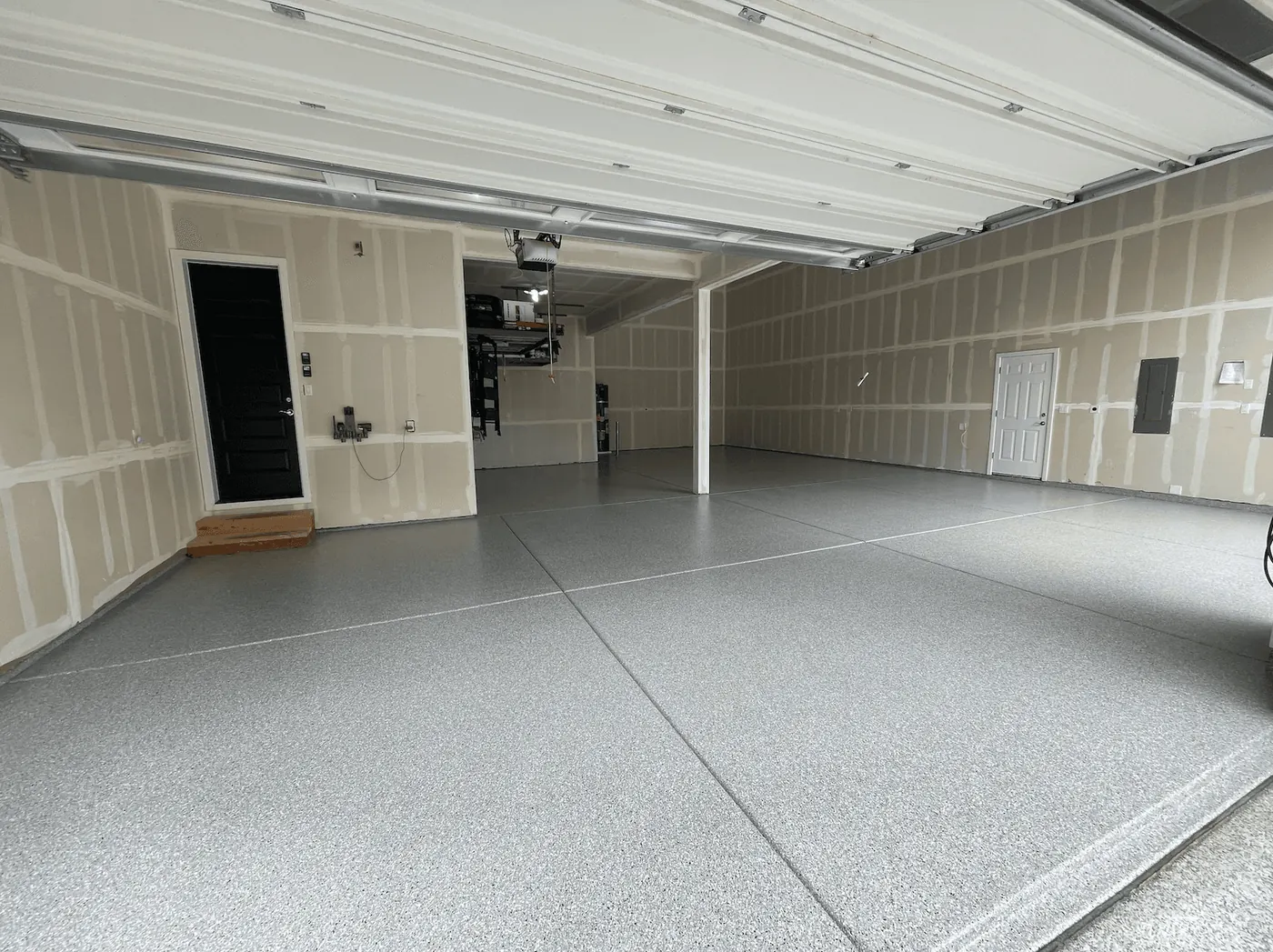 Dove gray flake floor in a new Seattle-area garage with taped drywall and a black entry door