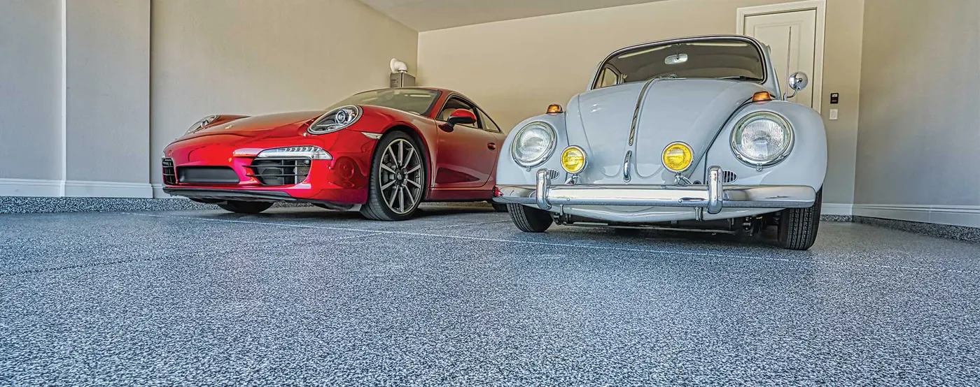 Red Porsche 911 and pale blue VW Beetle parked on a gray flake garage floor