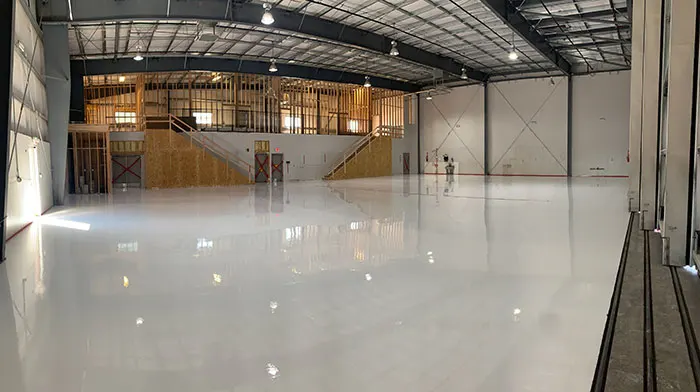 Large hangar with a bright white high-gloss floor and a mezzanine under construction